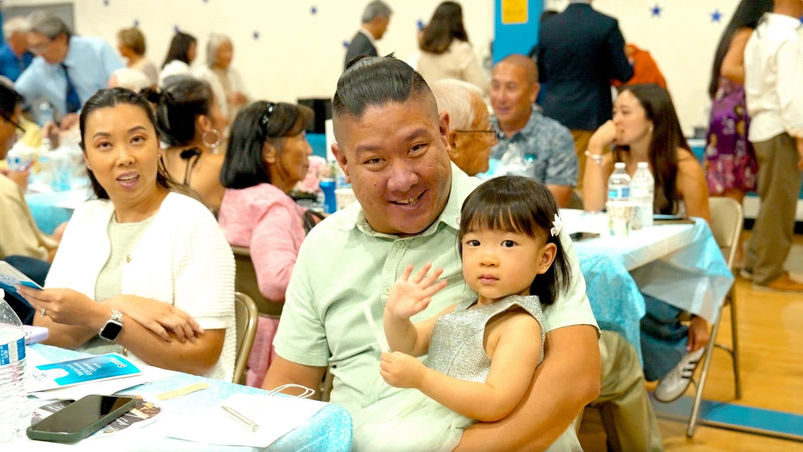 A father and his toddler waving from their table
