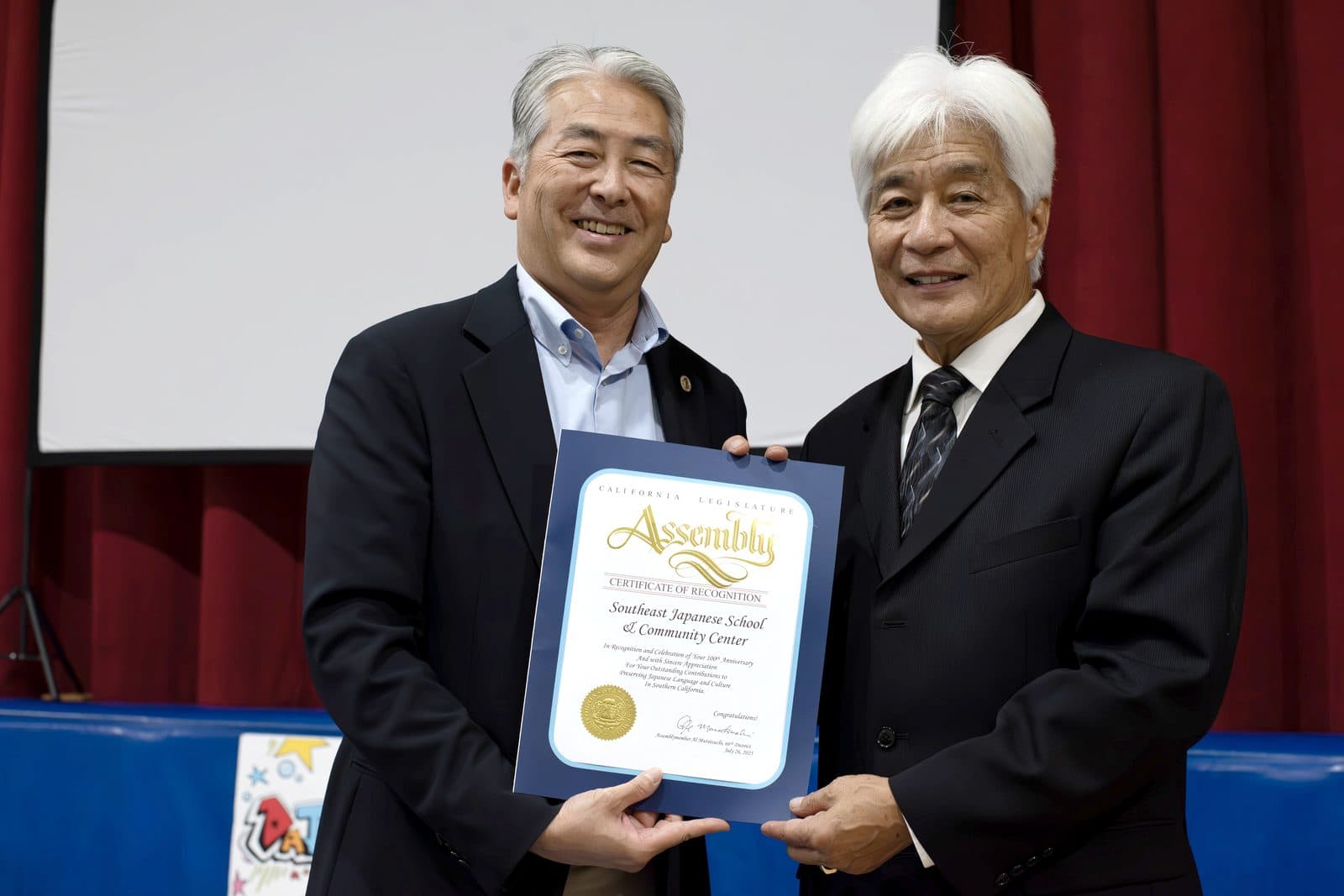 Two men in suits holding a framed proclamation honoring the center
